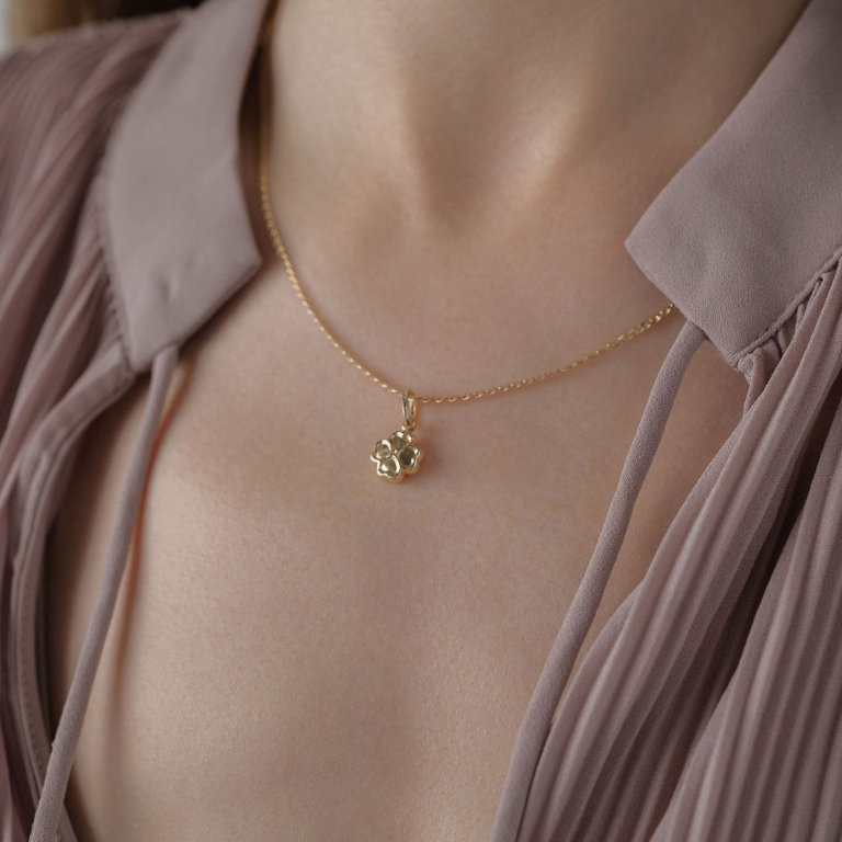 Gold necklace with a lucky charm pendant on a person wearing a light pink blouse.