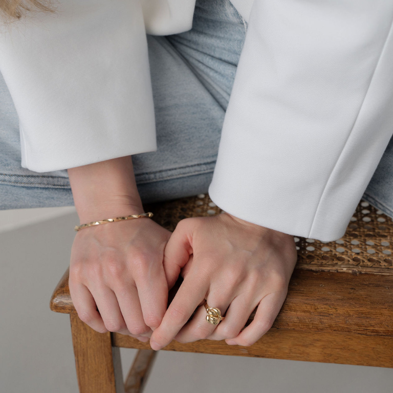 Close-up of hands with gold ring and bracelet on a wooden chair