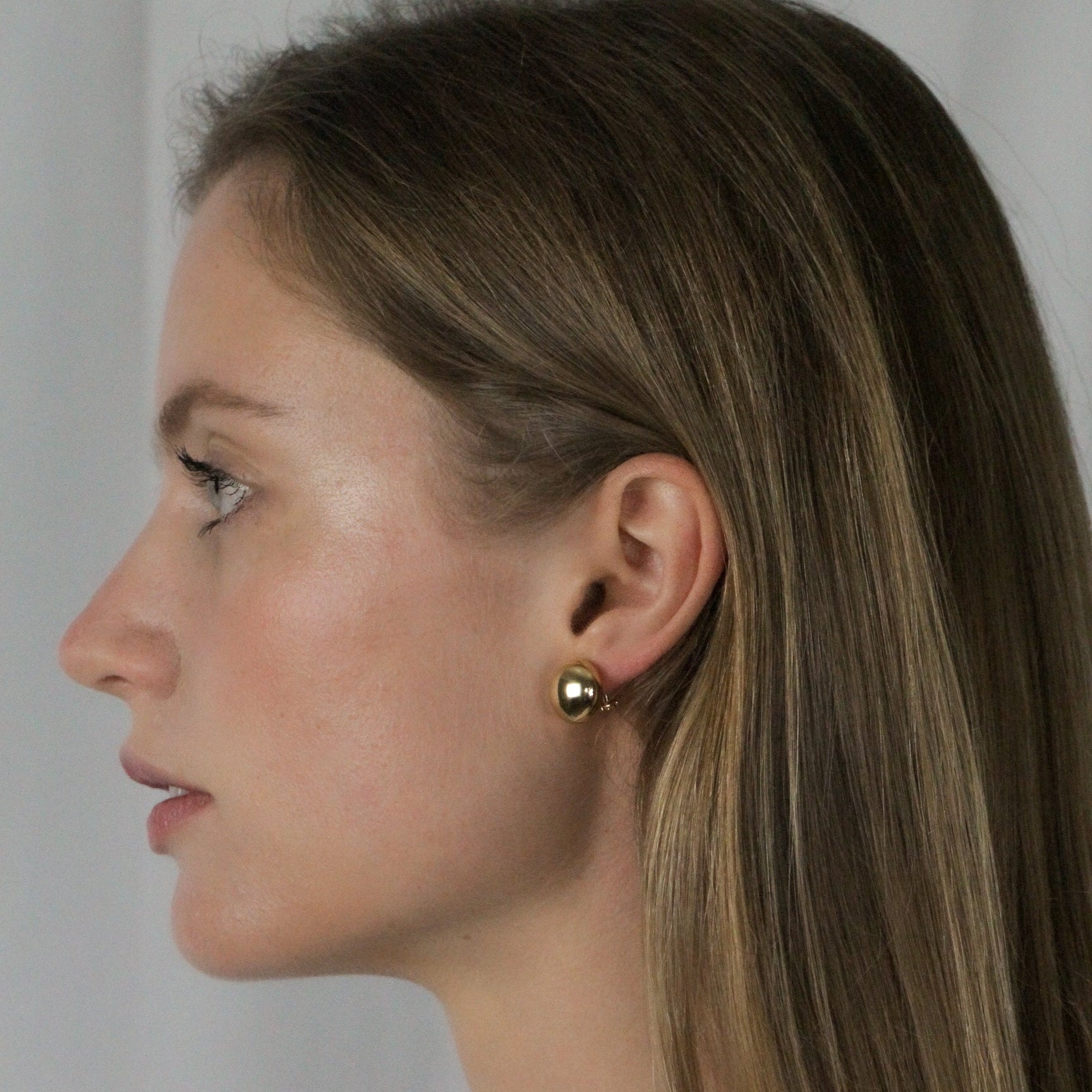 Woman wearing gold earrings against a plain background