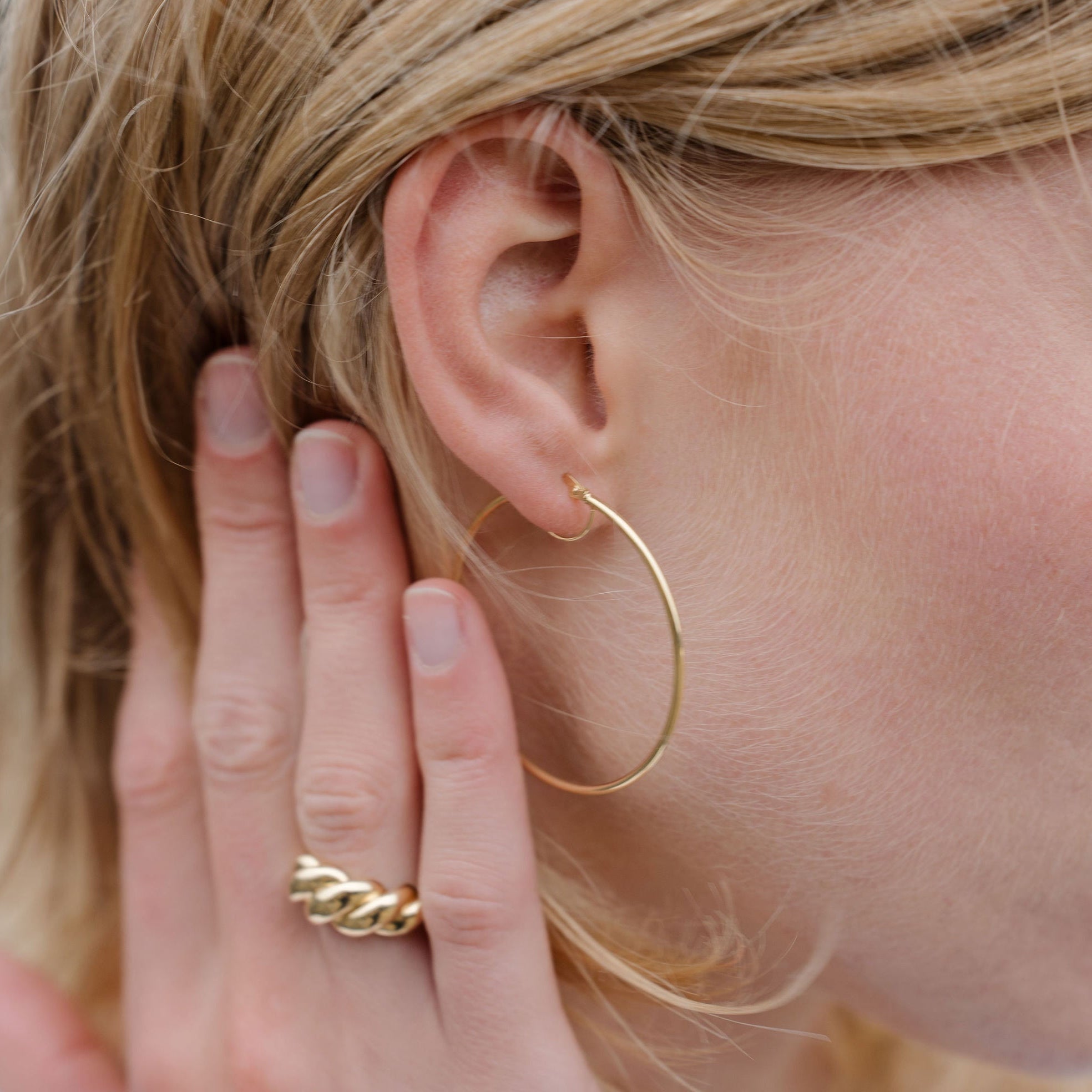 Close-up of a person wearing gold hoop earrings and a gold ring on a blurred background