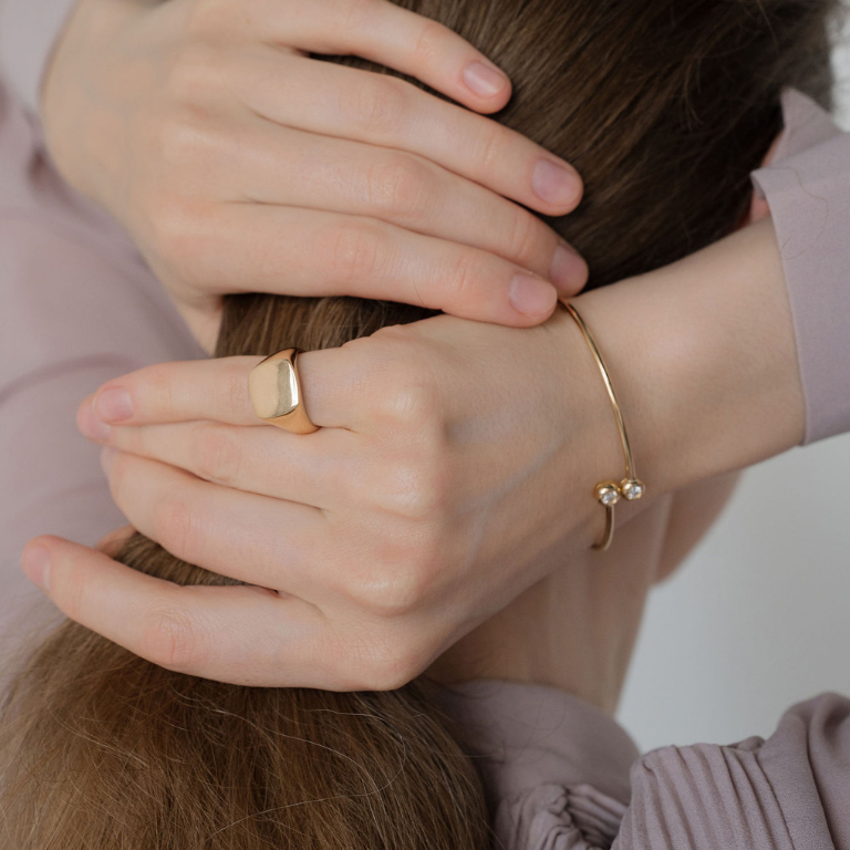 Close-up of hands with gold ring and bracelet on a neutral background