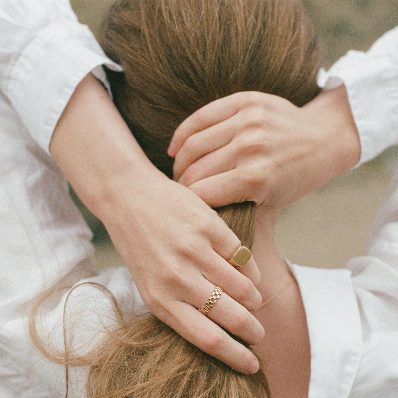 Person wearing gold rings with hands in hair on the beach
