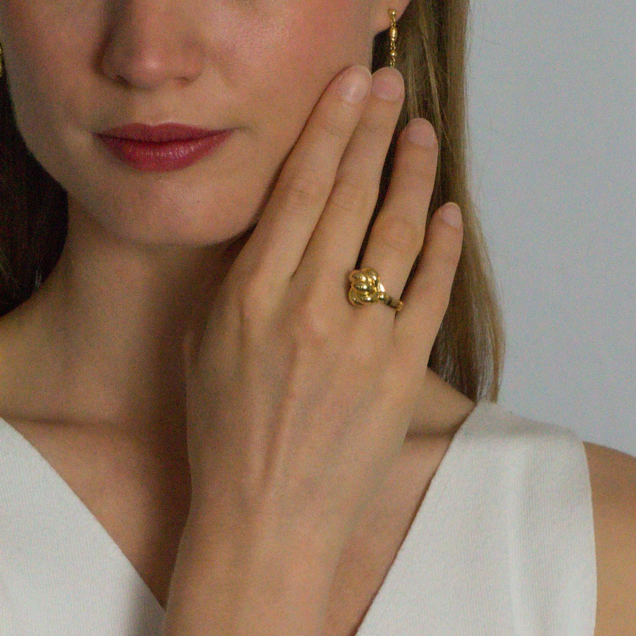 Close-up of a person wearing gold jewelry including an earring and ring, with a neutral background.