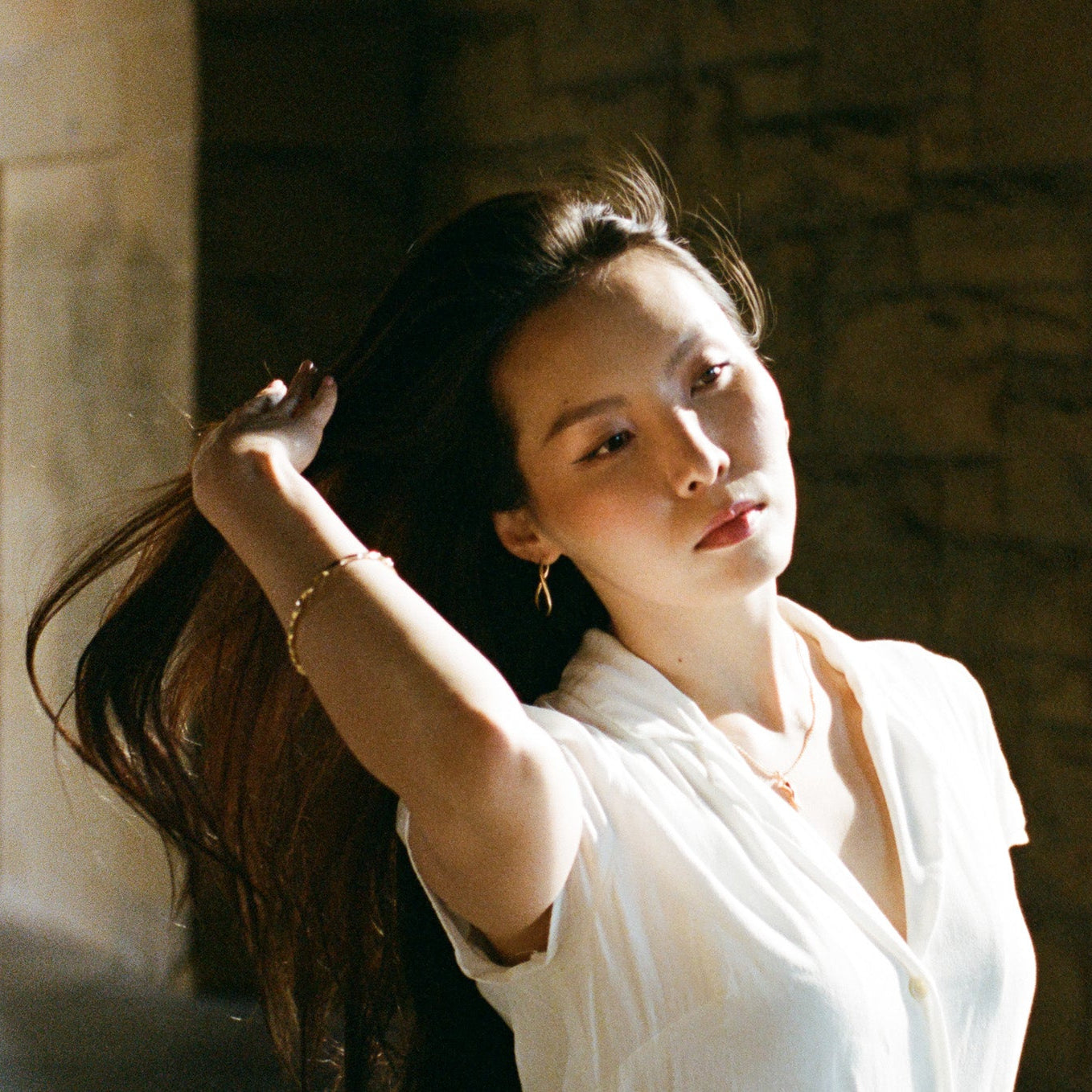Woman with gold jewelry standing in a stone corridor.