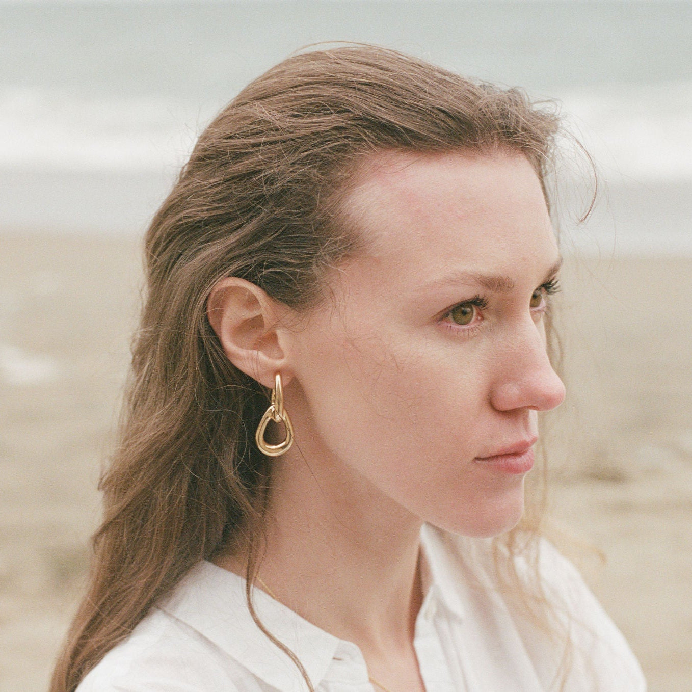 Woman wearing gold earrings on a beach