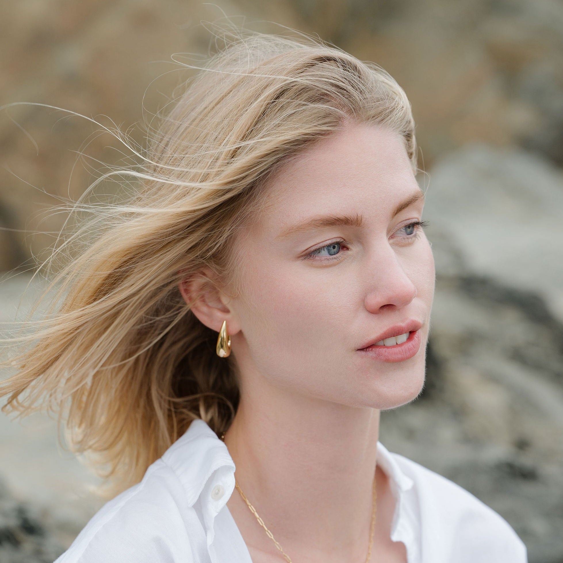 Woman with blonde hair and a white shirt standing against a rocky background