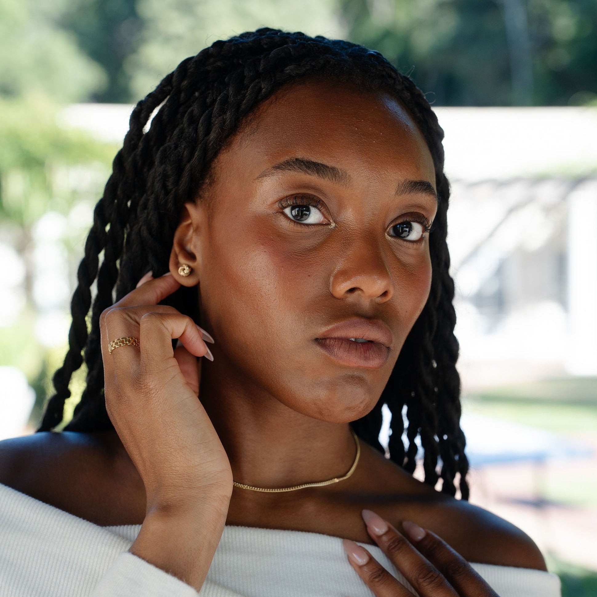 Model Wearing gold knot stud earrings and a white knit top.