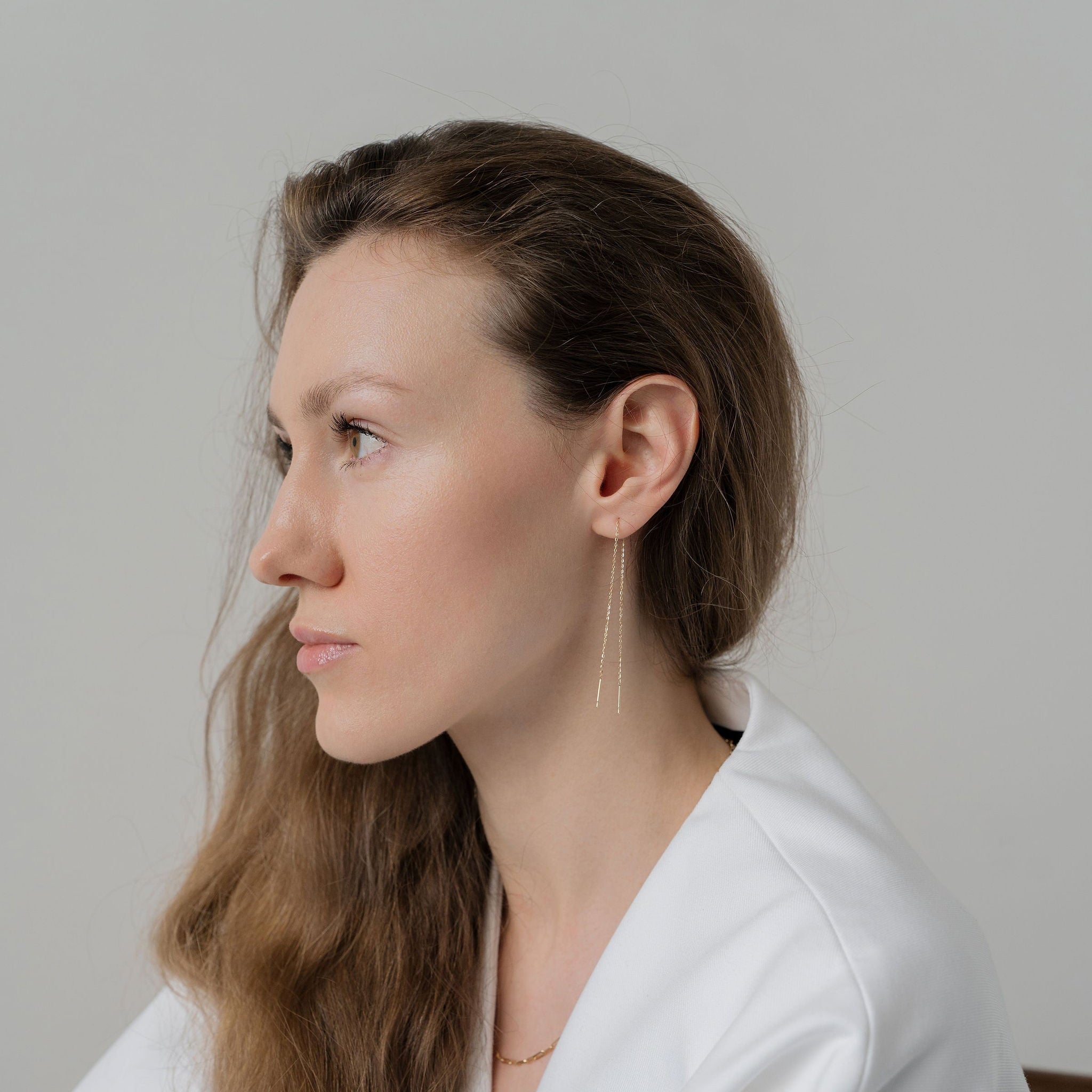 Woman wearing a white outfit with long hair, sitting against a plain background