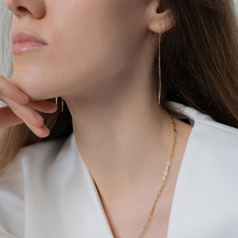 Close-up of a woman wearing gold earrings and a necklace, with a neutral background.