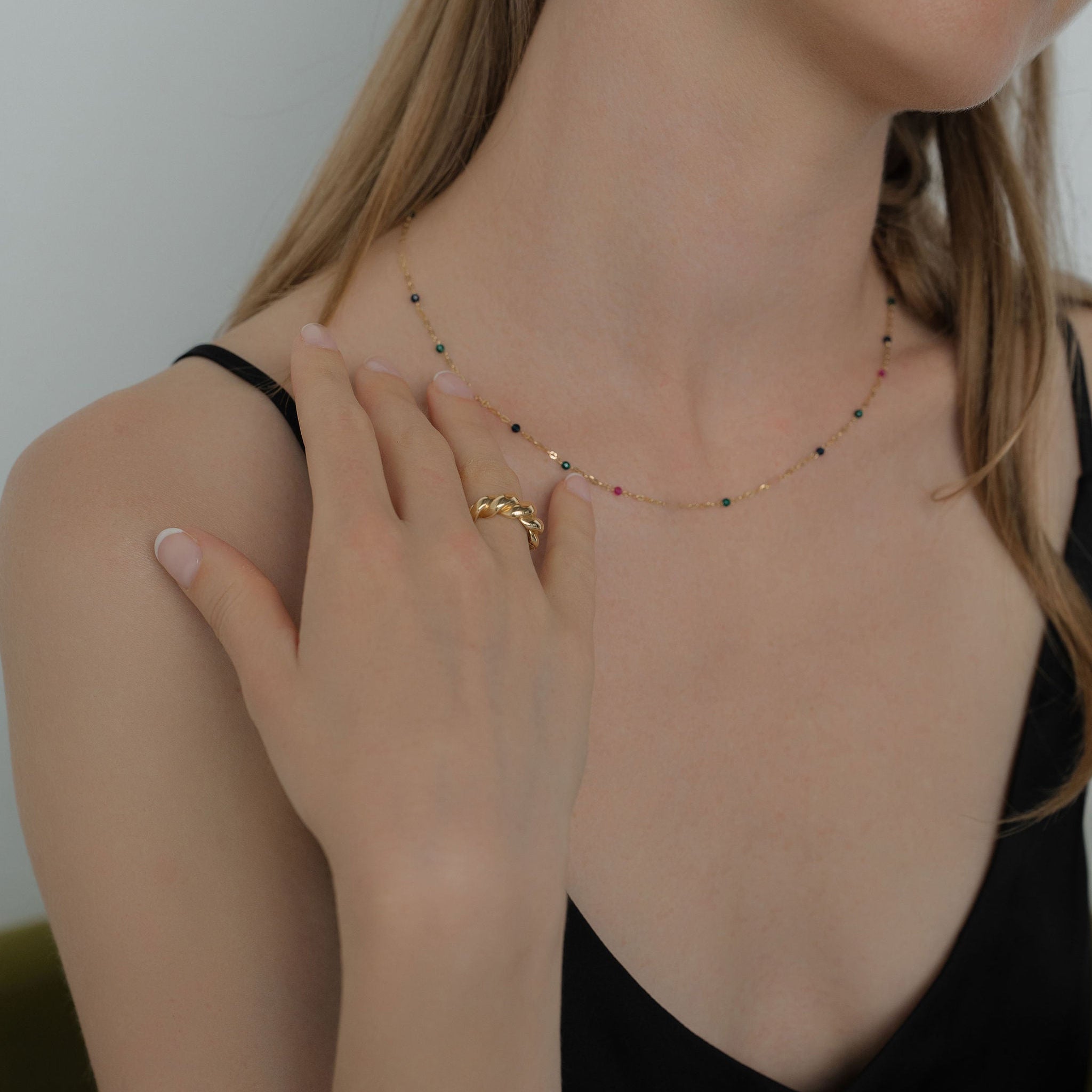 Woman wearing gold jewelry including a necklace, ring, and bracelet against a neutral background